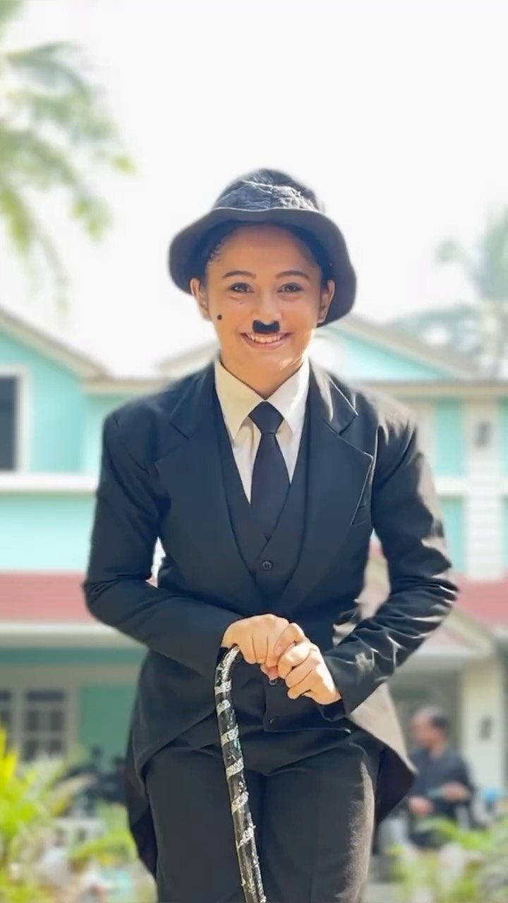 A woman in a black suit and hat with a painted mustache holding a cane.