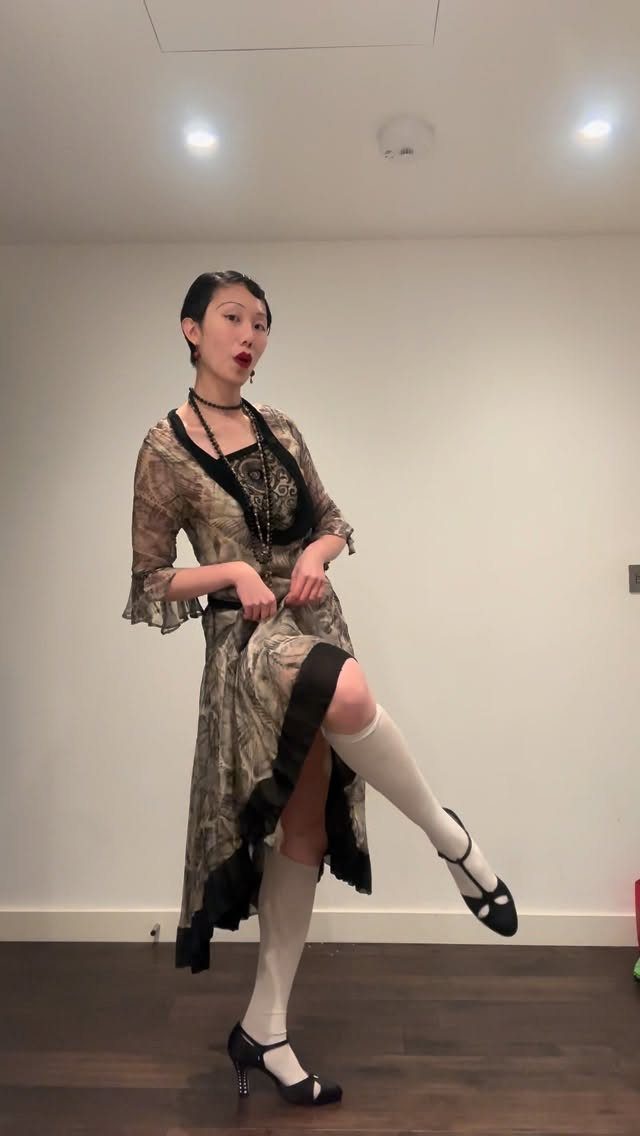 A woman posing in a vintage patterned dress with black lace and white knee-high socks.