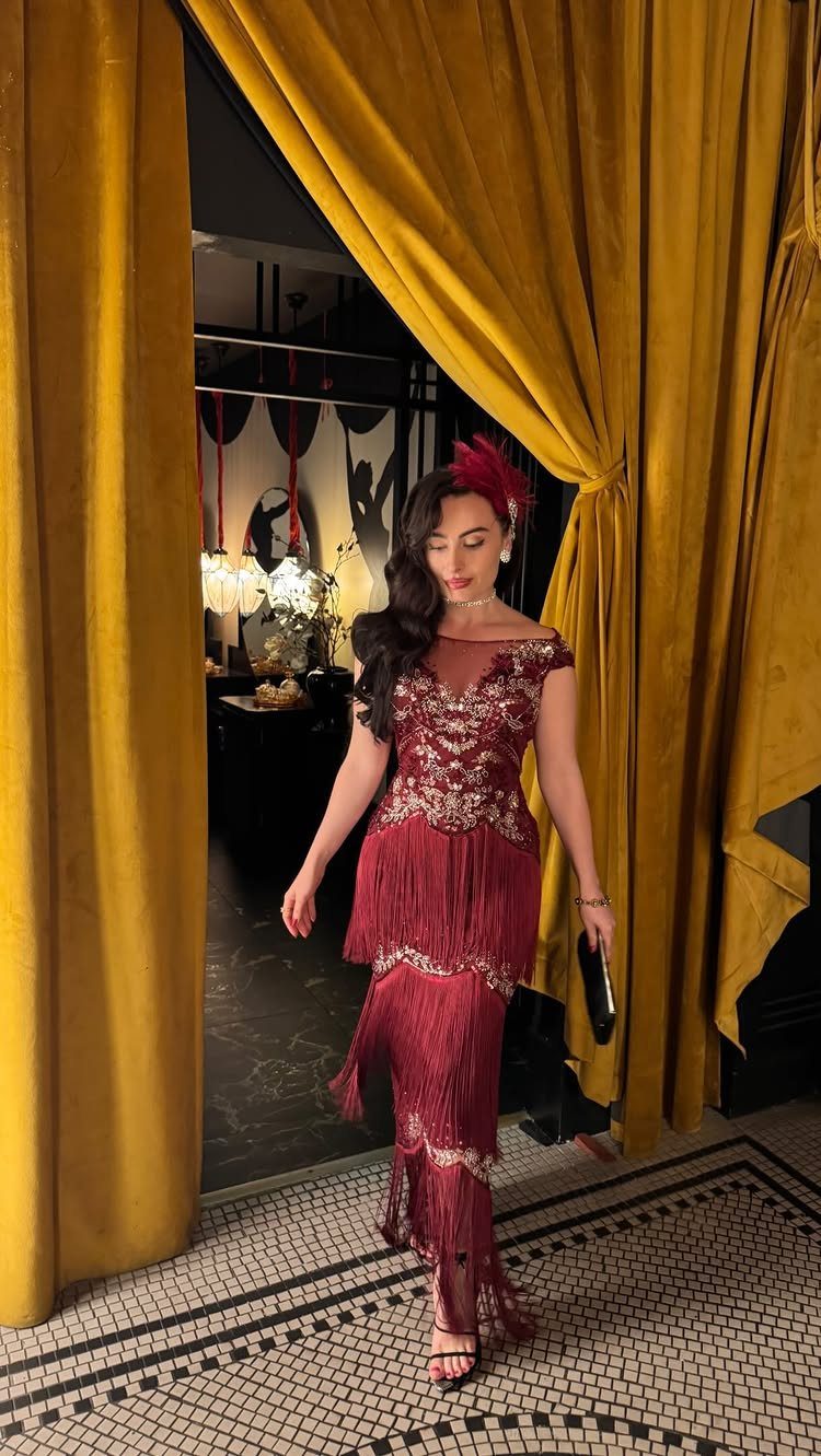 Woman in a red sequined fringe gown walking through yellow velvet curtains.