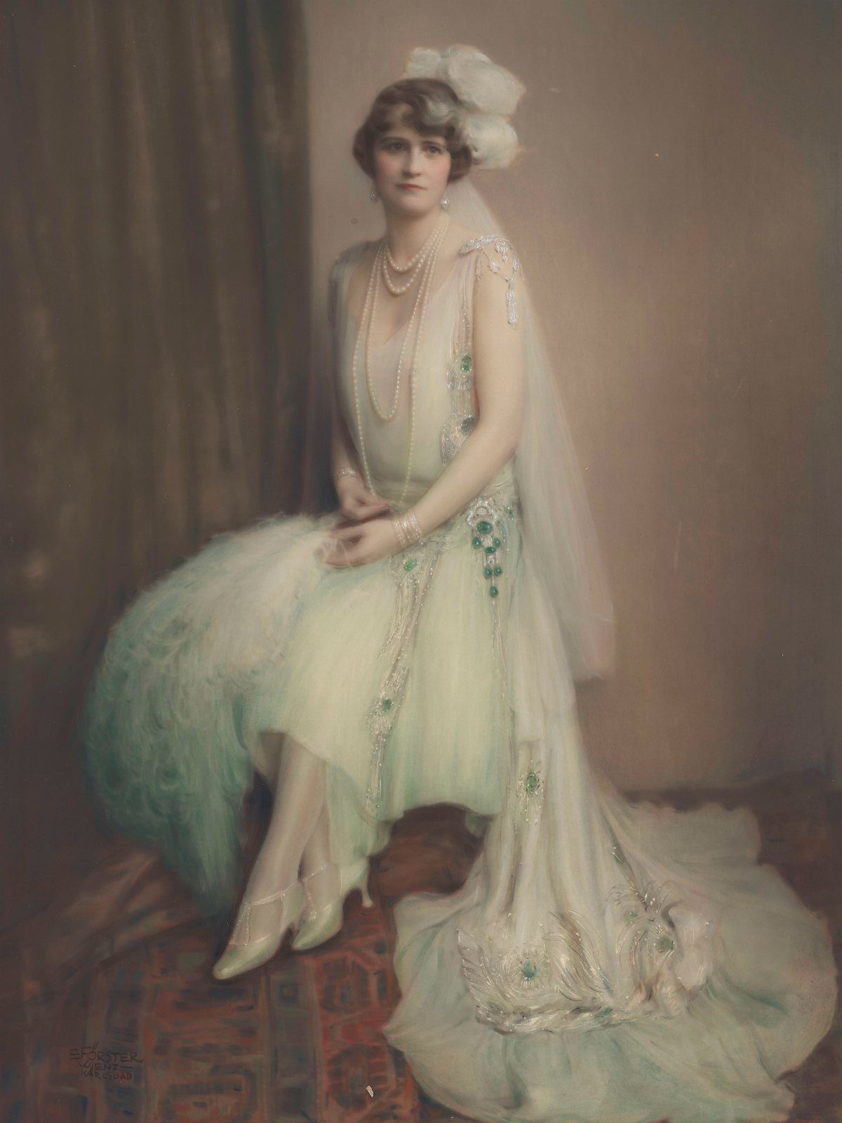 A woman wearing a beaded 1920s evening dress with a long train and white headpiece.