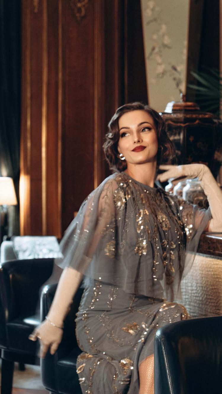 Woman in a grey sequined chiffon flapper dress sitting in an elegant room.