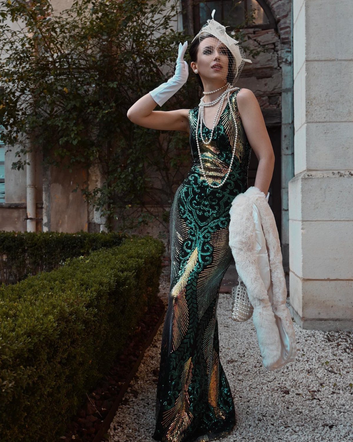 Woman in a green sequined flapper dress posing with white gloves and a fur stole.
