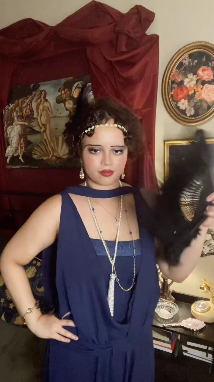 A woman in a navy blue flapper-style dress posing with a black feather fan.