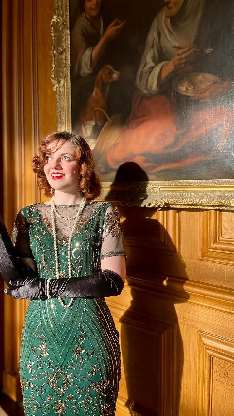 Woman in a green beaded dress wearing long black gloves and a pearl necklace.