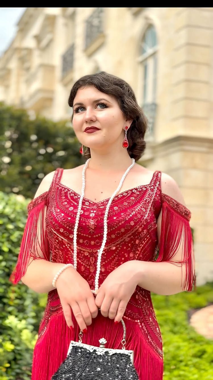 Woman in a red fringed flapper dress with pearls and a black sequined clutch.