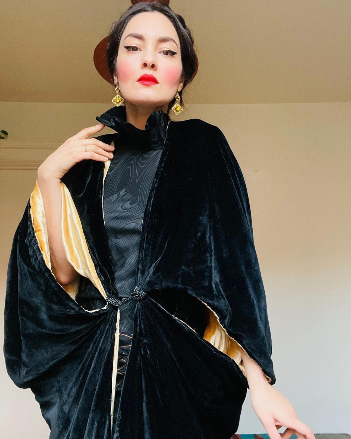 Woman in a black velvet cocoon coat with yellow lining and gold earrings.