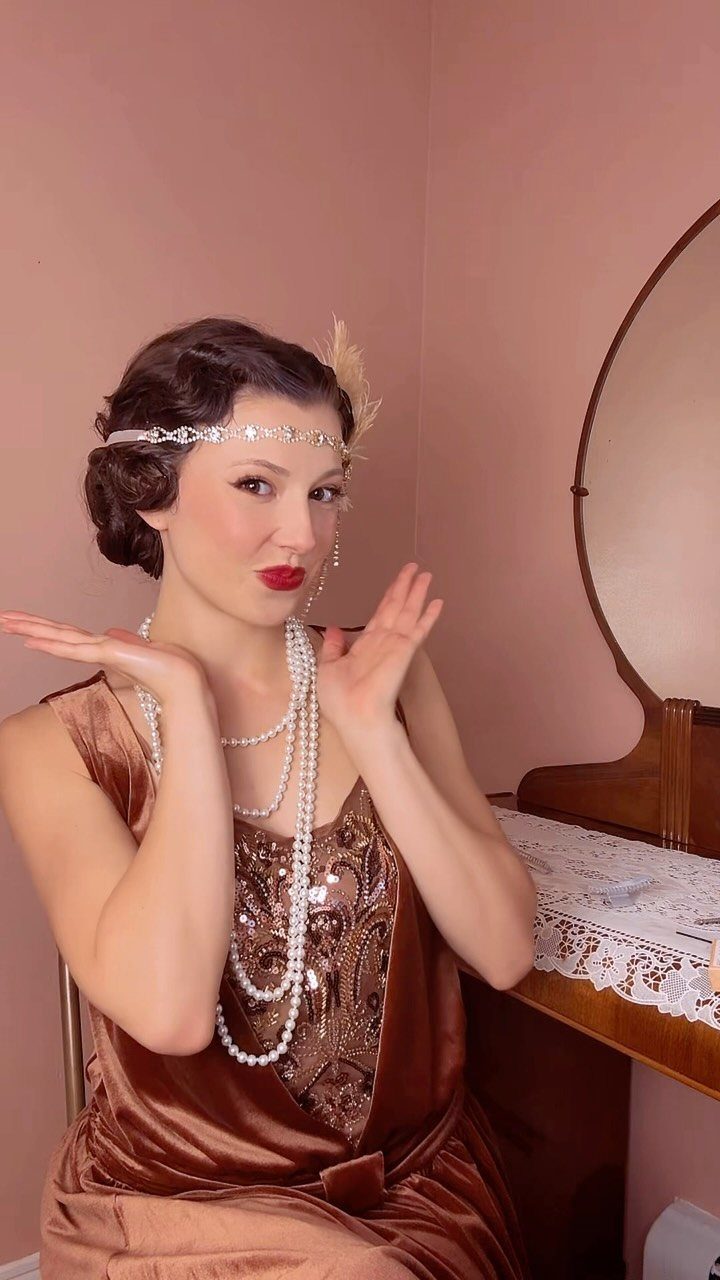 Woman in 1920s flapper attire wearing a beaded headband and feather hair accessory.