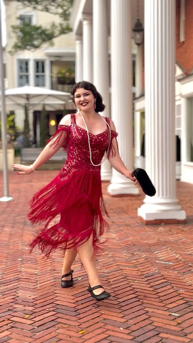 A woman in a red sequined flapper dress with fringe posing on a brick path.