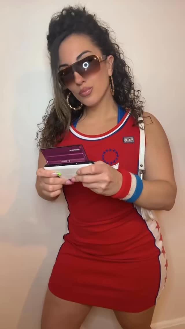 A woman in a red mini dress and large sunglasses holding a small purple device.
