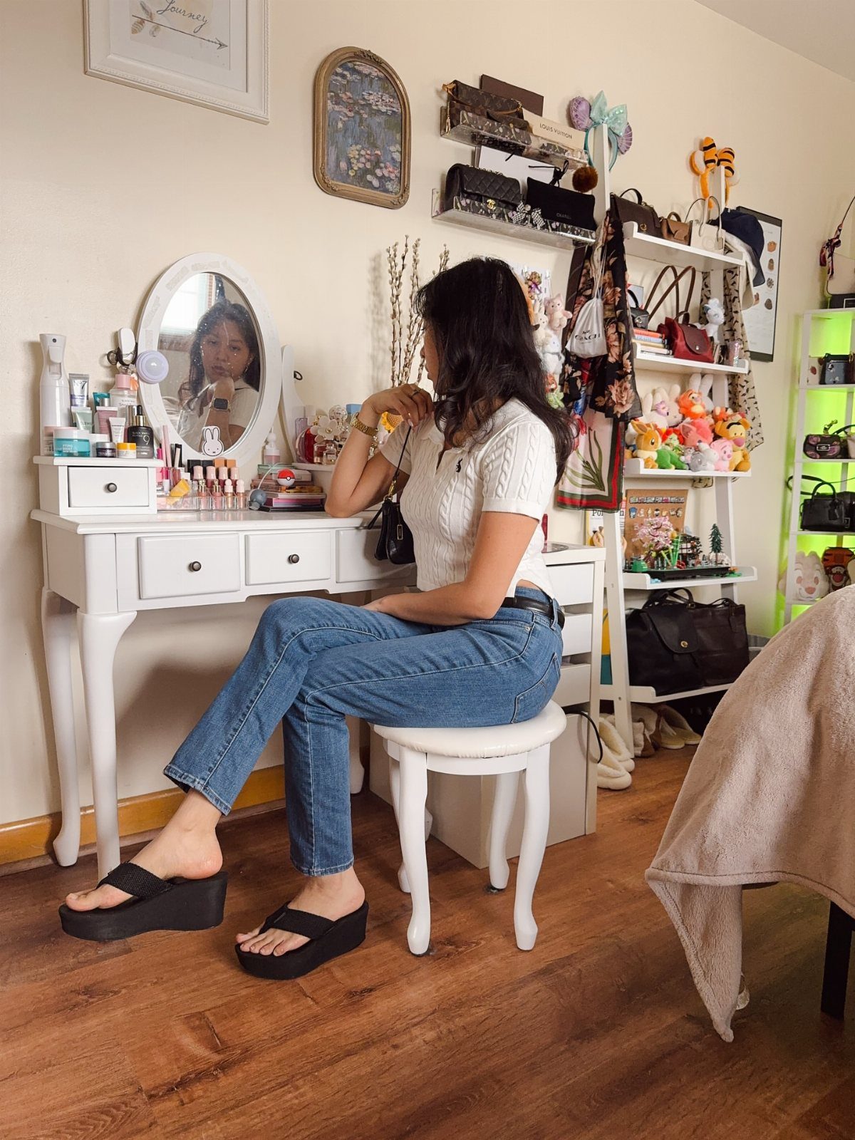Woman in white top and blue jeans wearing black platform flip-flops while sitting at a vanity.