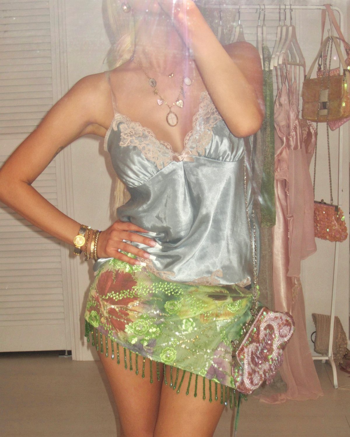 A person wearing a light blue satin camisole with lace trim and a green sequined skirt.