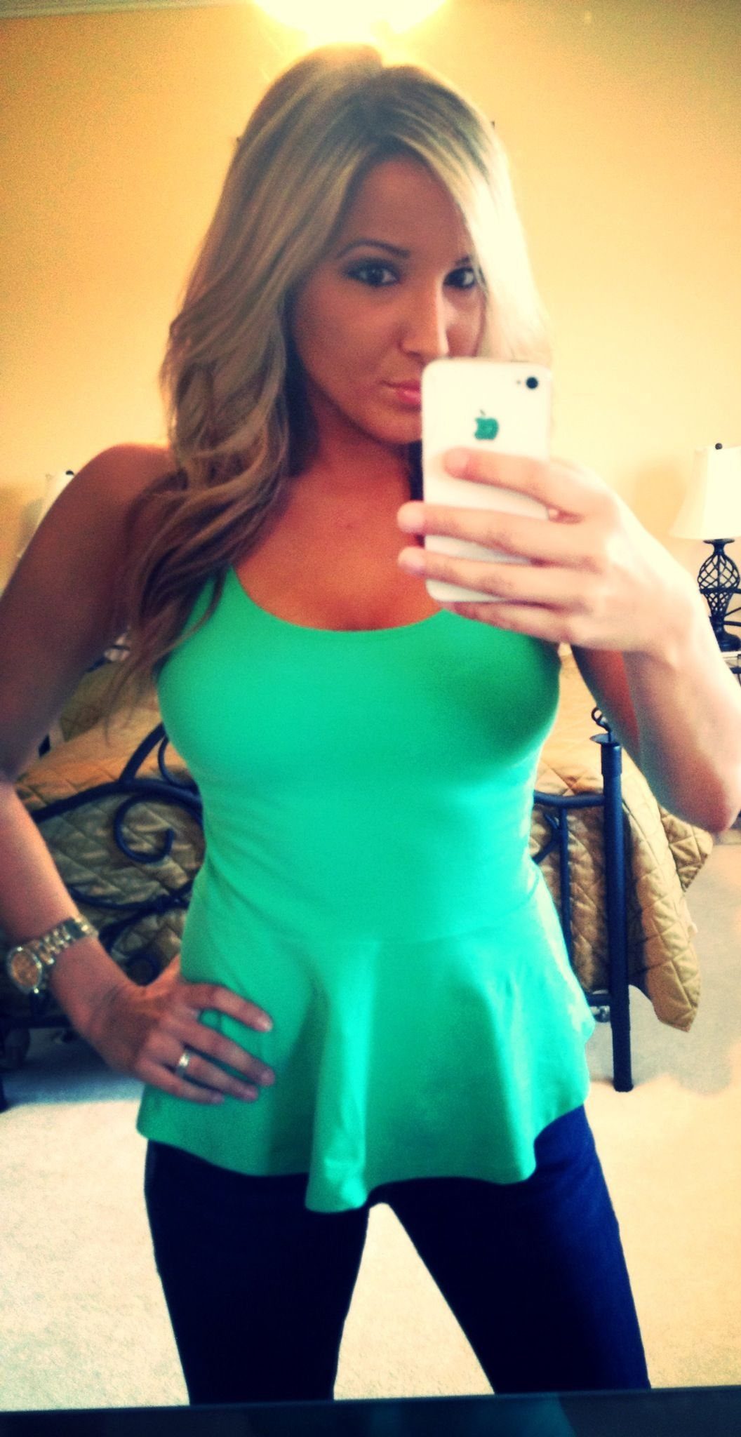 A blonde woman posing in a mirror wearing a bright green sleeveless peplum top.