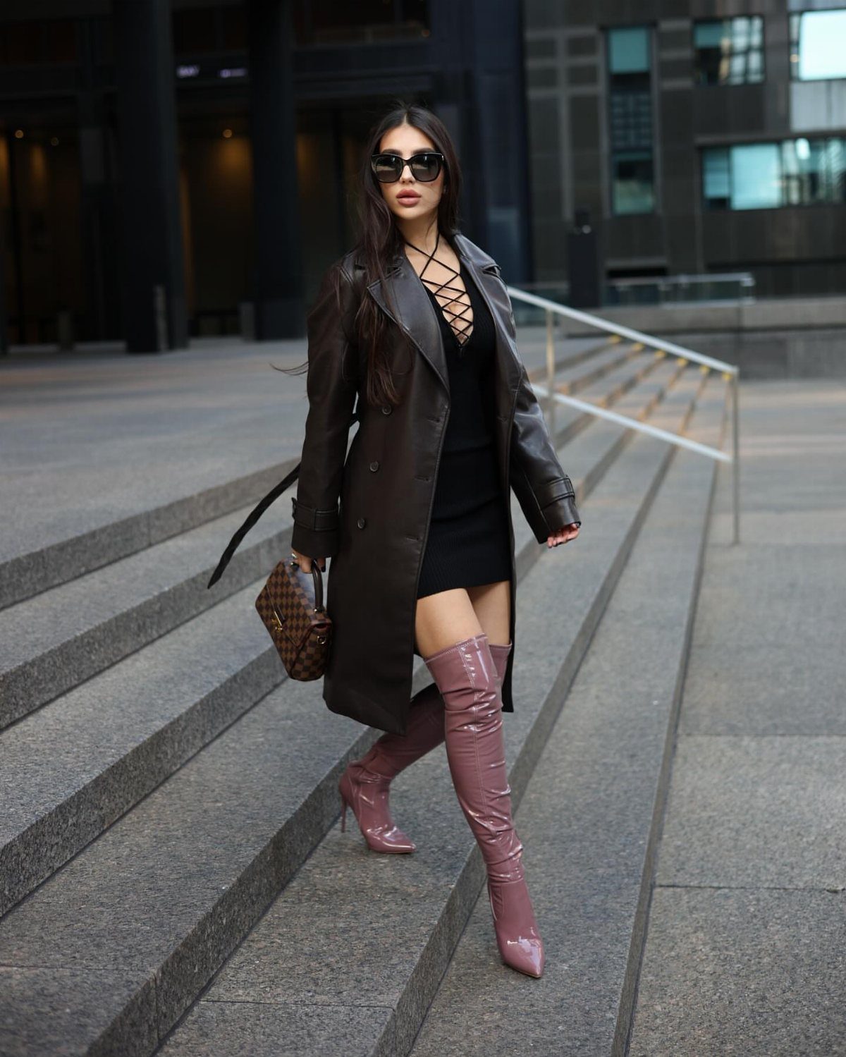 A woman in a leather coat and mauve over-the-knee boots walking down outdoor stone stairs.