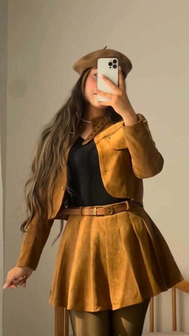 Woman wearing a tan suede jacket, matching flared skirt, and a brown beret while taking a selfie.