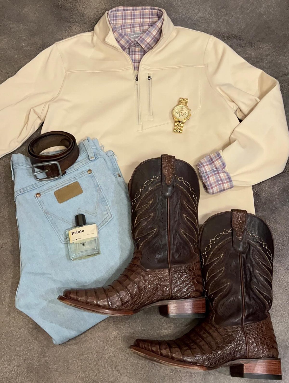 Flat lay of a cream pullover, plaid shirt, light blue jeans, brown cowboy boots, and accessories.