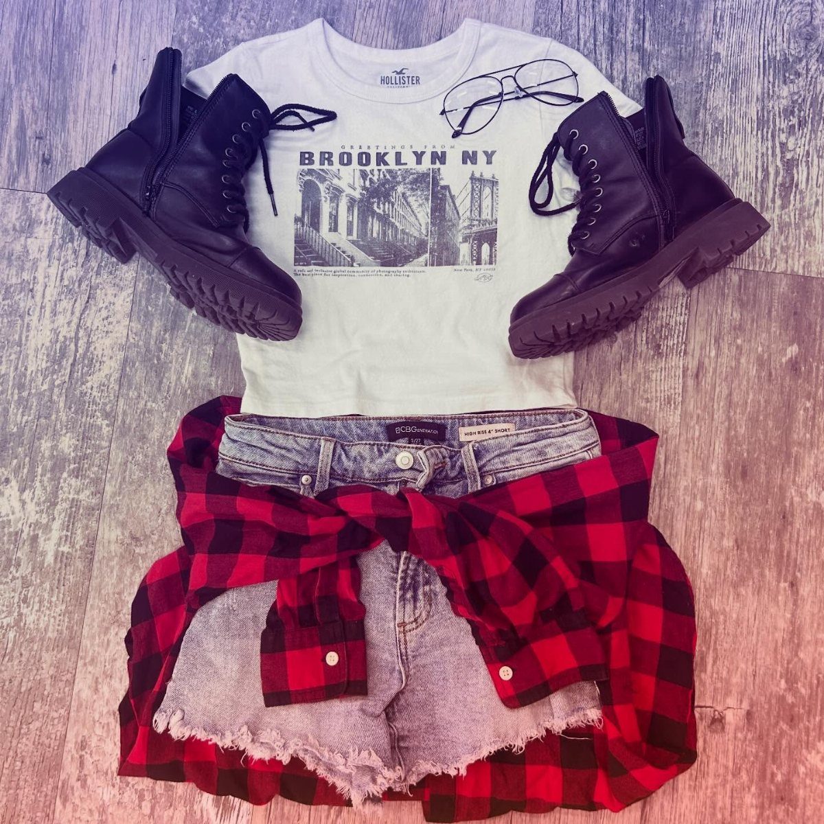 Flat lay of a white graphic t-shirt, denim shorts, red flannel, and black combat boots.