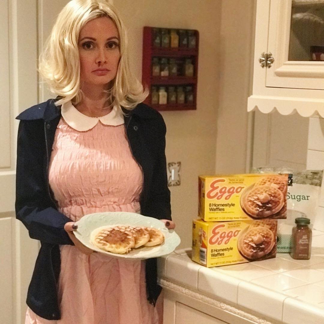 Blonde woman in a pink dress holding a plate of waffles next to Eggo boxes.
