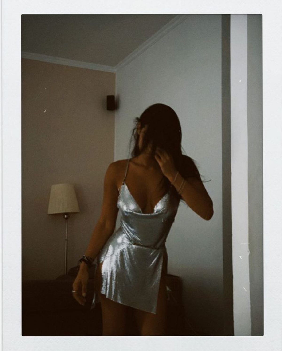 Woman in a shimmering silver metallic mini dress posing in a dimly lit room.