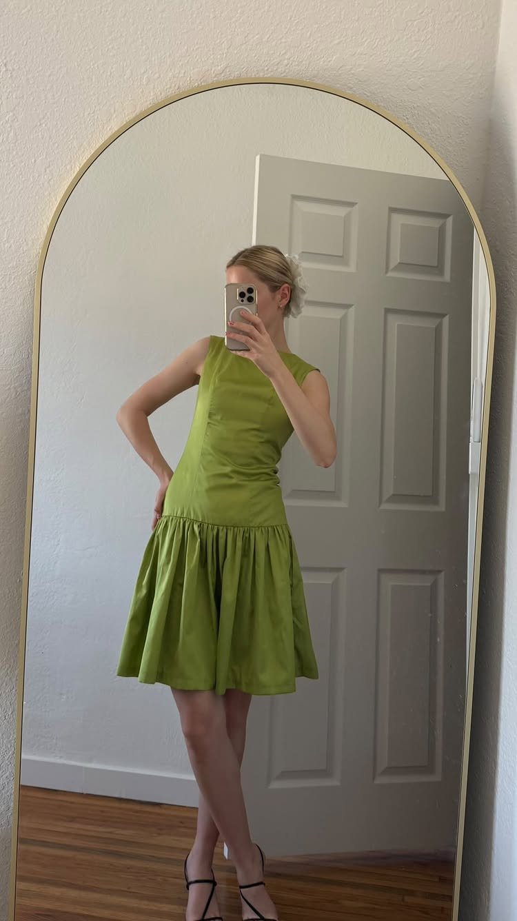 A woman in a lime green sleeveless dress with a low waistline posing in a mirror.