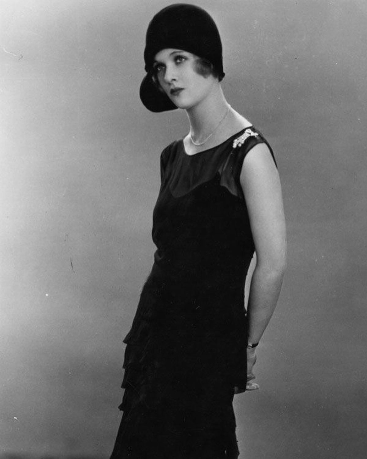 A woman wearing a black 1920s sleeveless dress and a matching cloche hat.