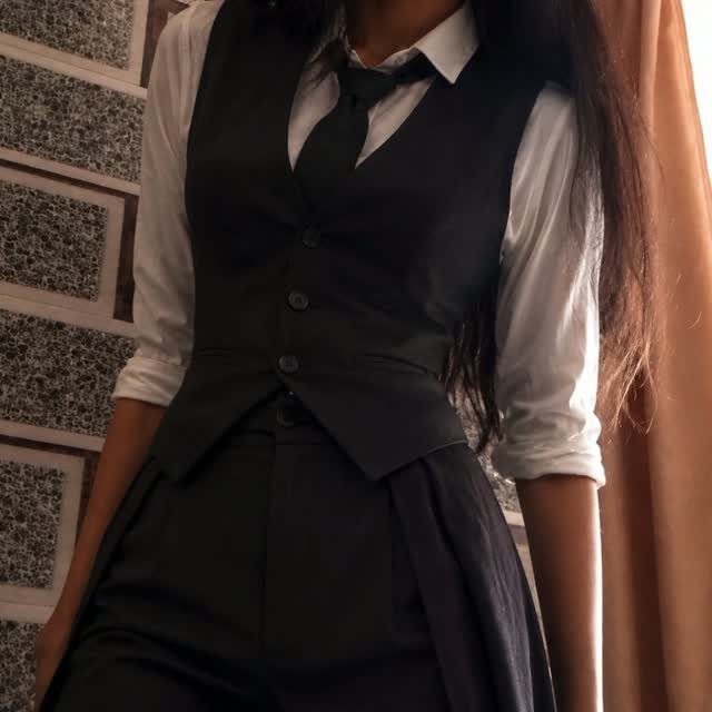 A person dressed in a white shirt, black tie, waistcoat, and trousers.