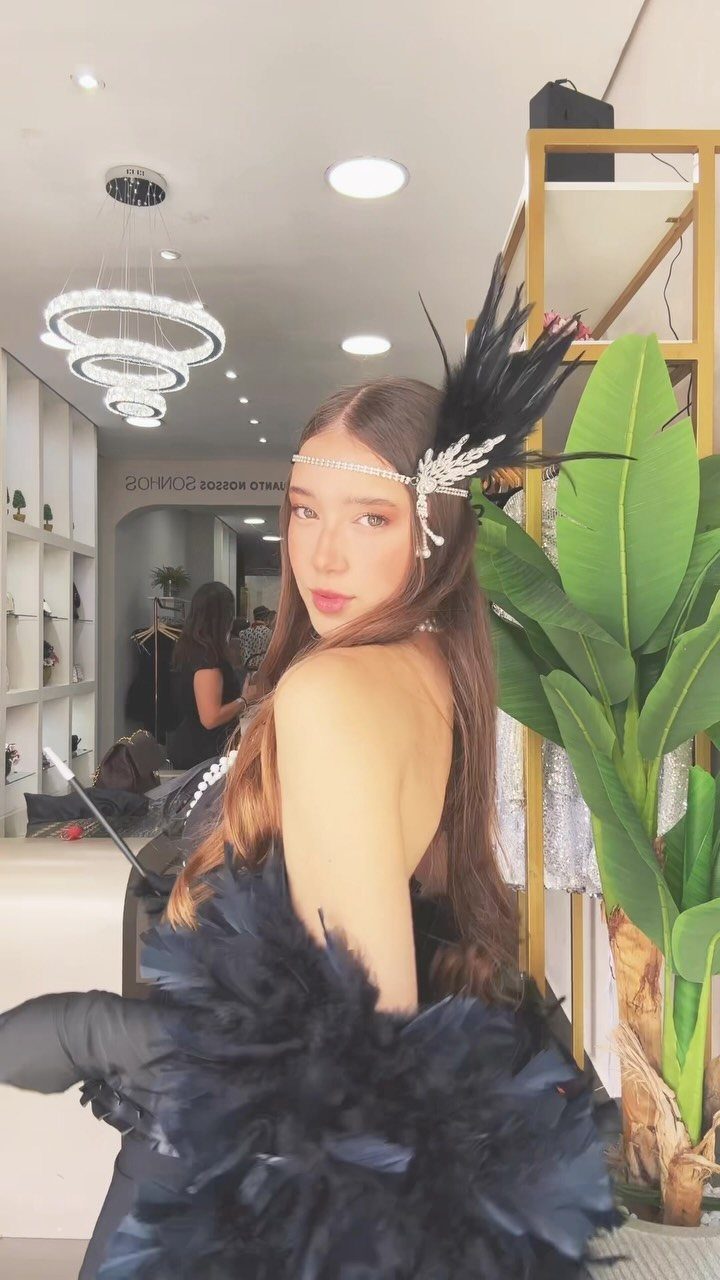 A woman wearing a black feathered headpiece and black feathered clothing posing indoors.