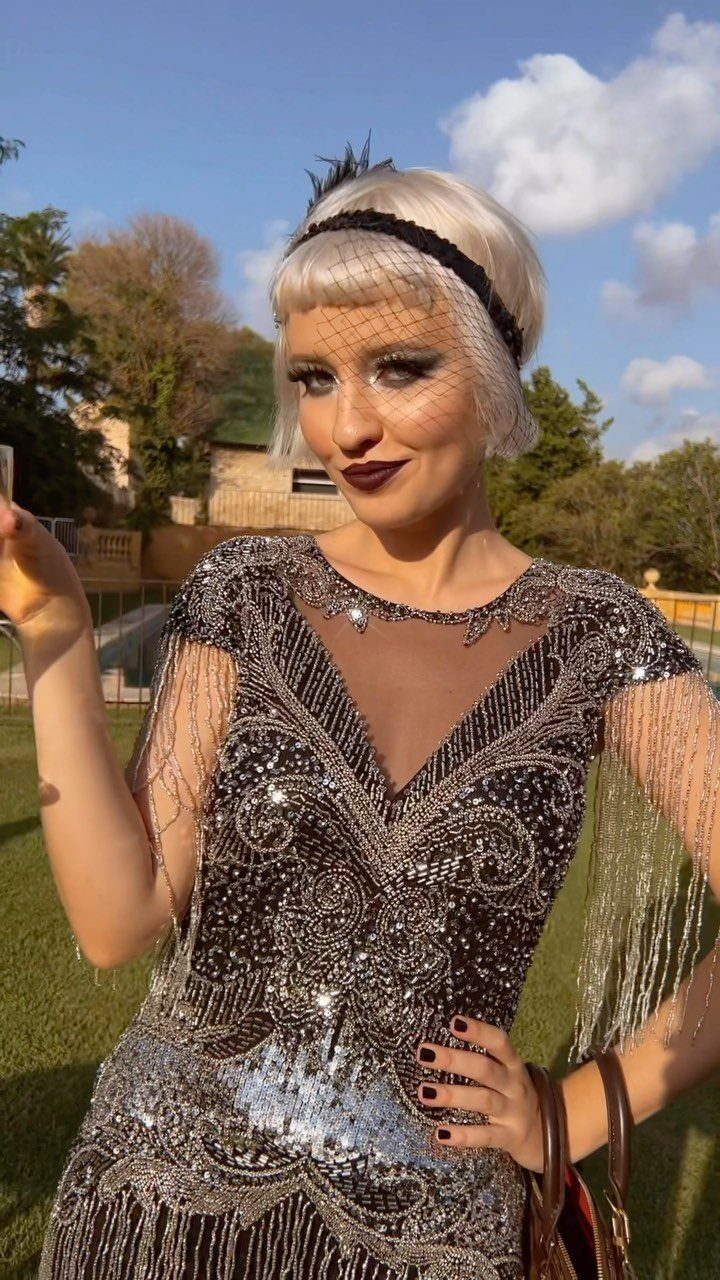 A woman wearing a beaded black flapper dress with fringe and a headband outdoors.