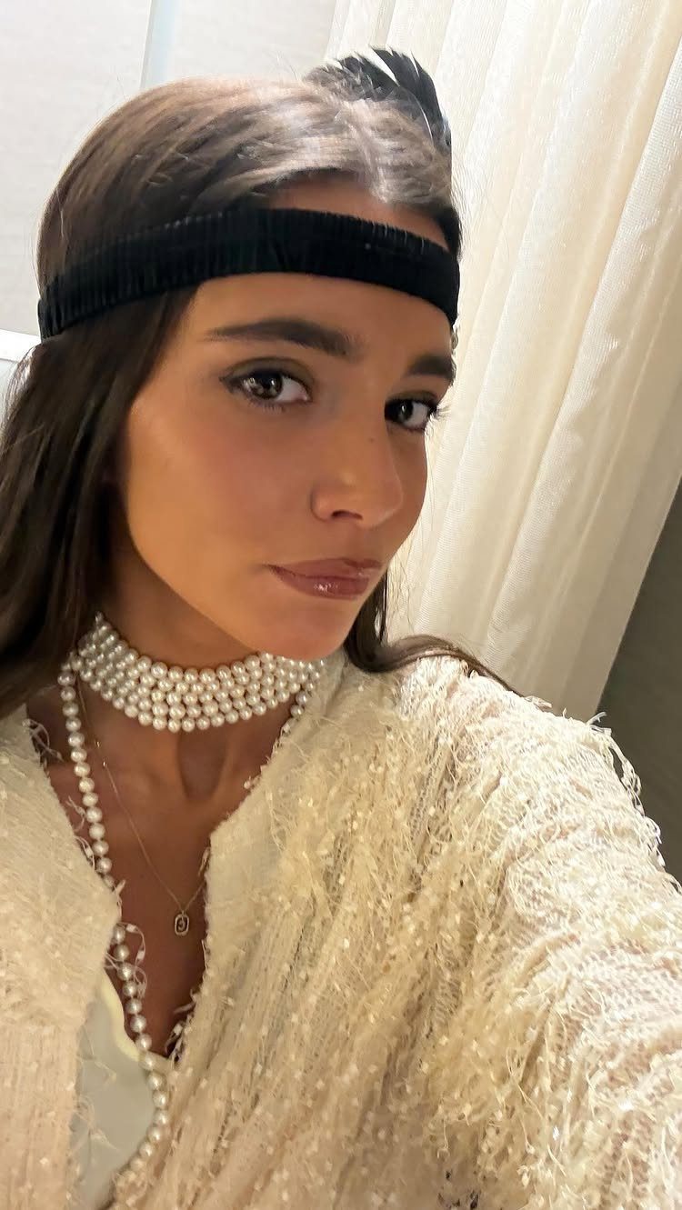 A woman wearing a black headband and pearl necklaces in a 1920s style outfit.