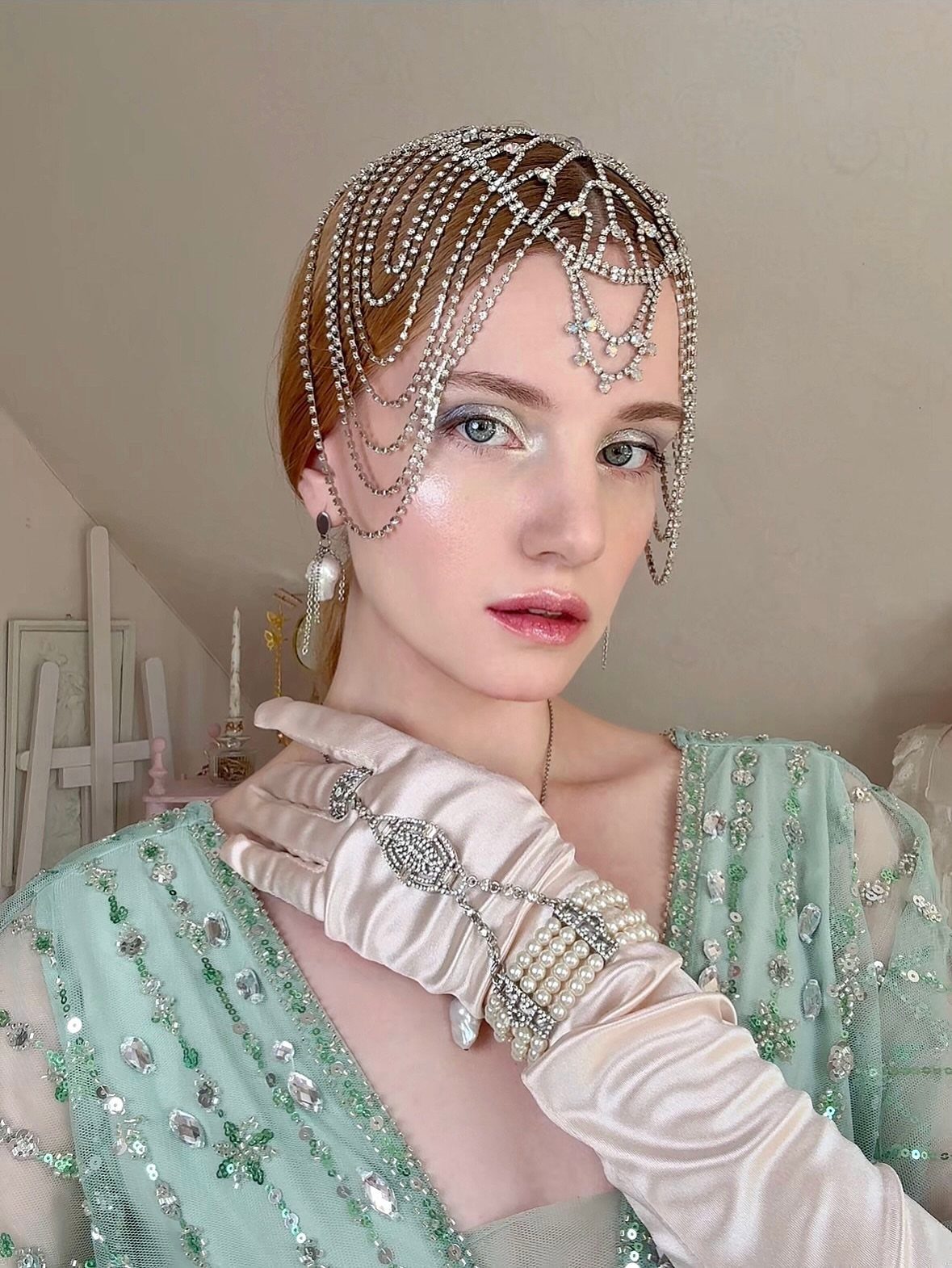 Woman wearing a beaded headpiece, statement earrings, and long satin gloves with pearl jewelry.