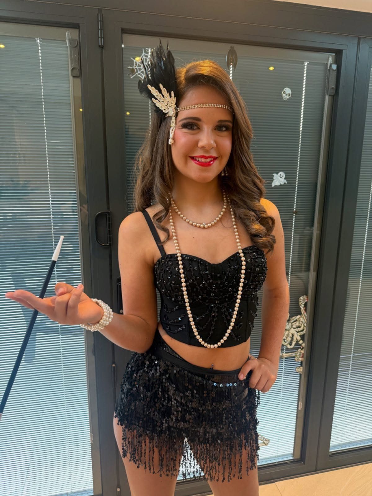 A woman in a black sequined flapper outfit and pearl accessories posing indoors.