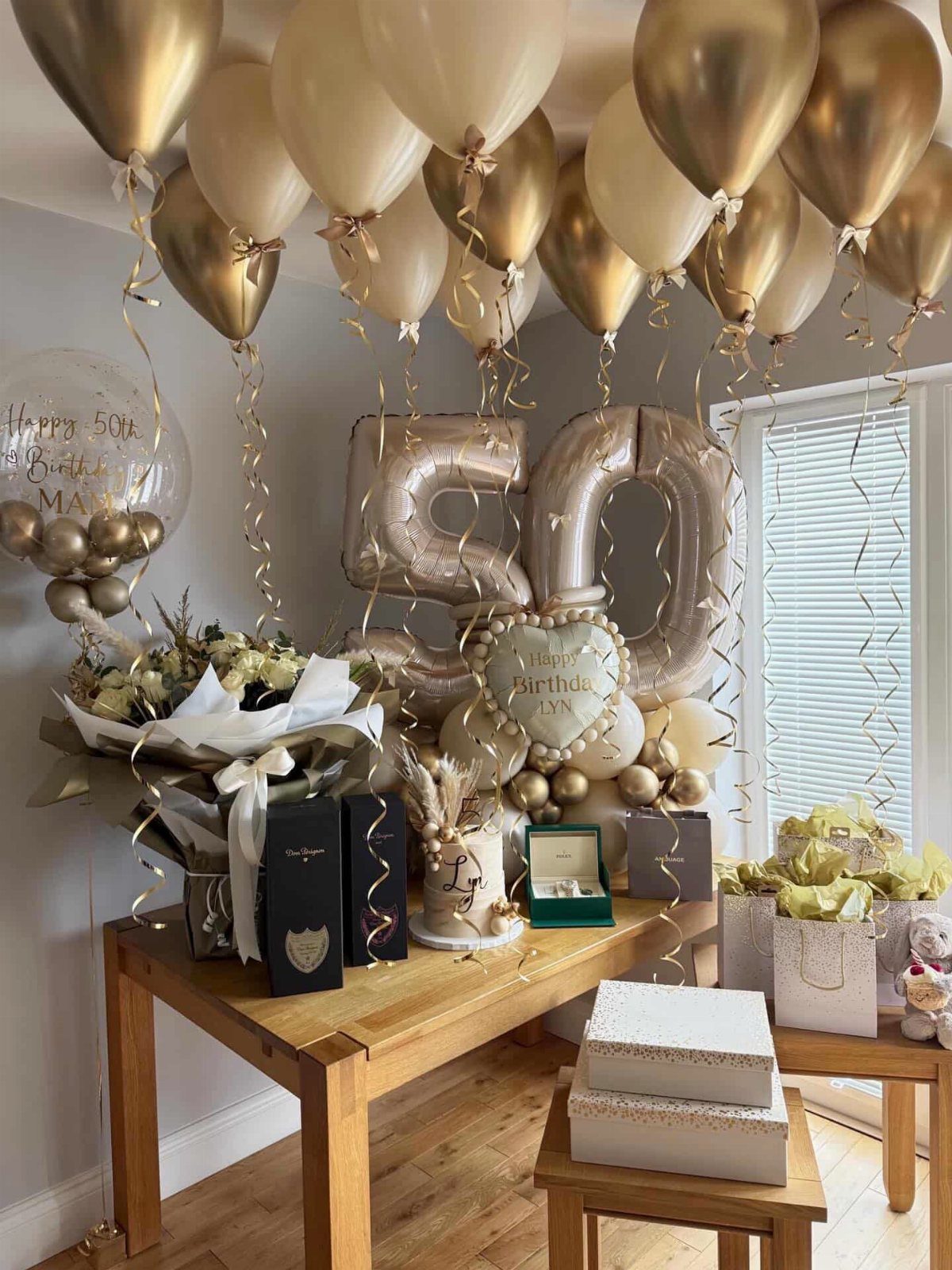 Gold and cream balloons decorate a table with large number 50 balloons and gifts.