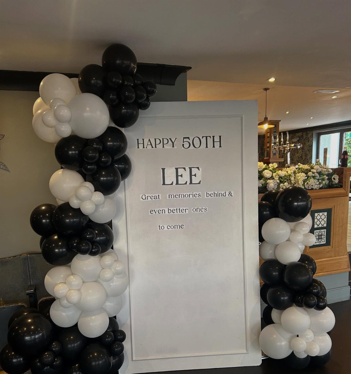 A white sign celebrating Lee's 50th birthday framed by black and white balloon garlands.
