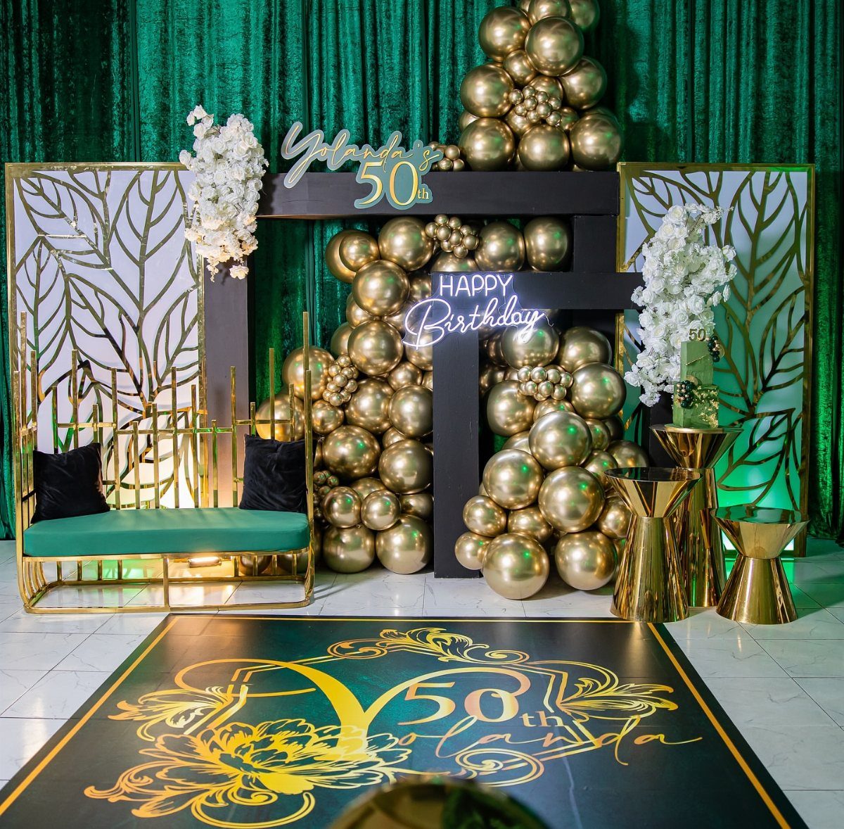 Gold and black balloon decorations surrounding a green velvet backdrop and a custom 50th birthday dance floor.