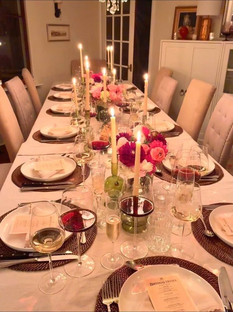An elegant long dining table set with candles, flowers, and wine glasses for a dinner party.