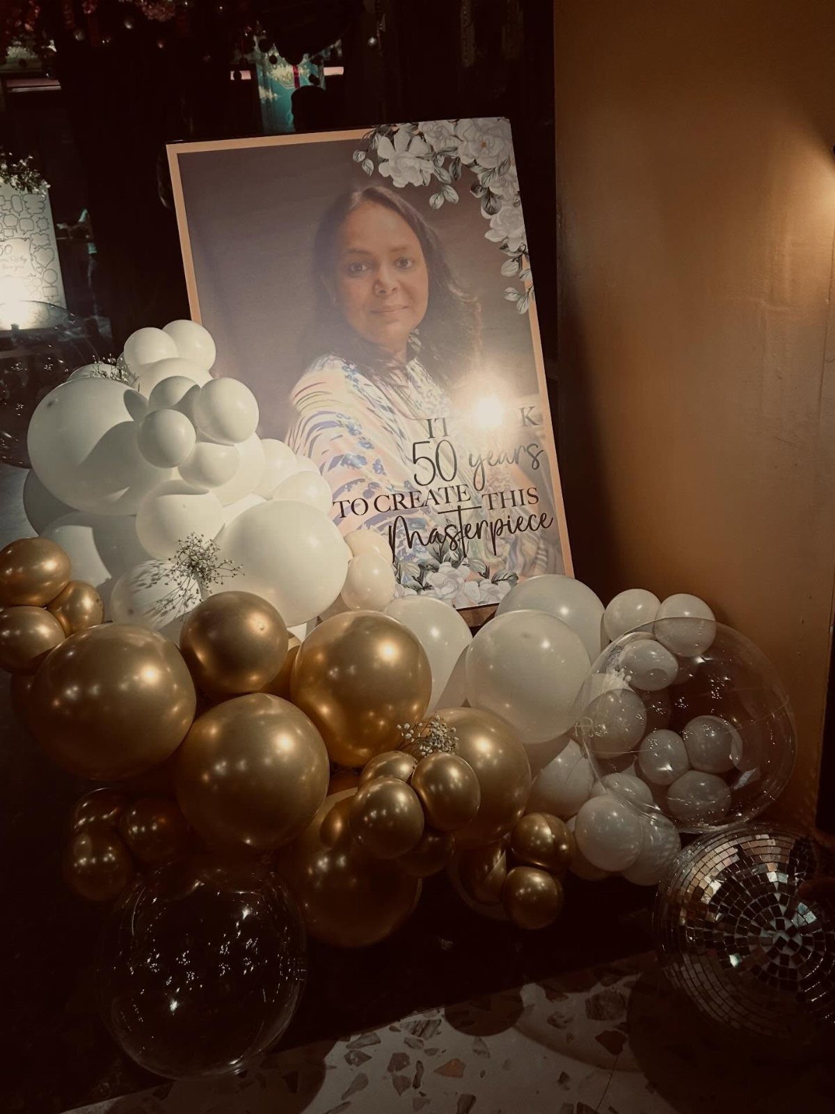 A large portrait sign with gold and white balloons and a disco ball.