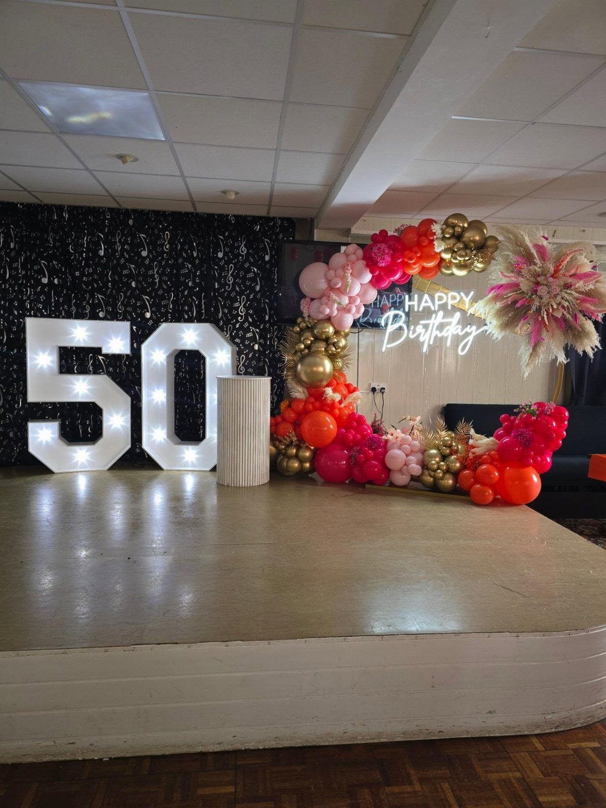 Large illuminated number 50 and a colorful balloon arch with a neon birthday sign.