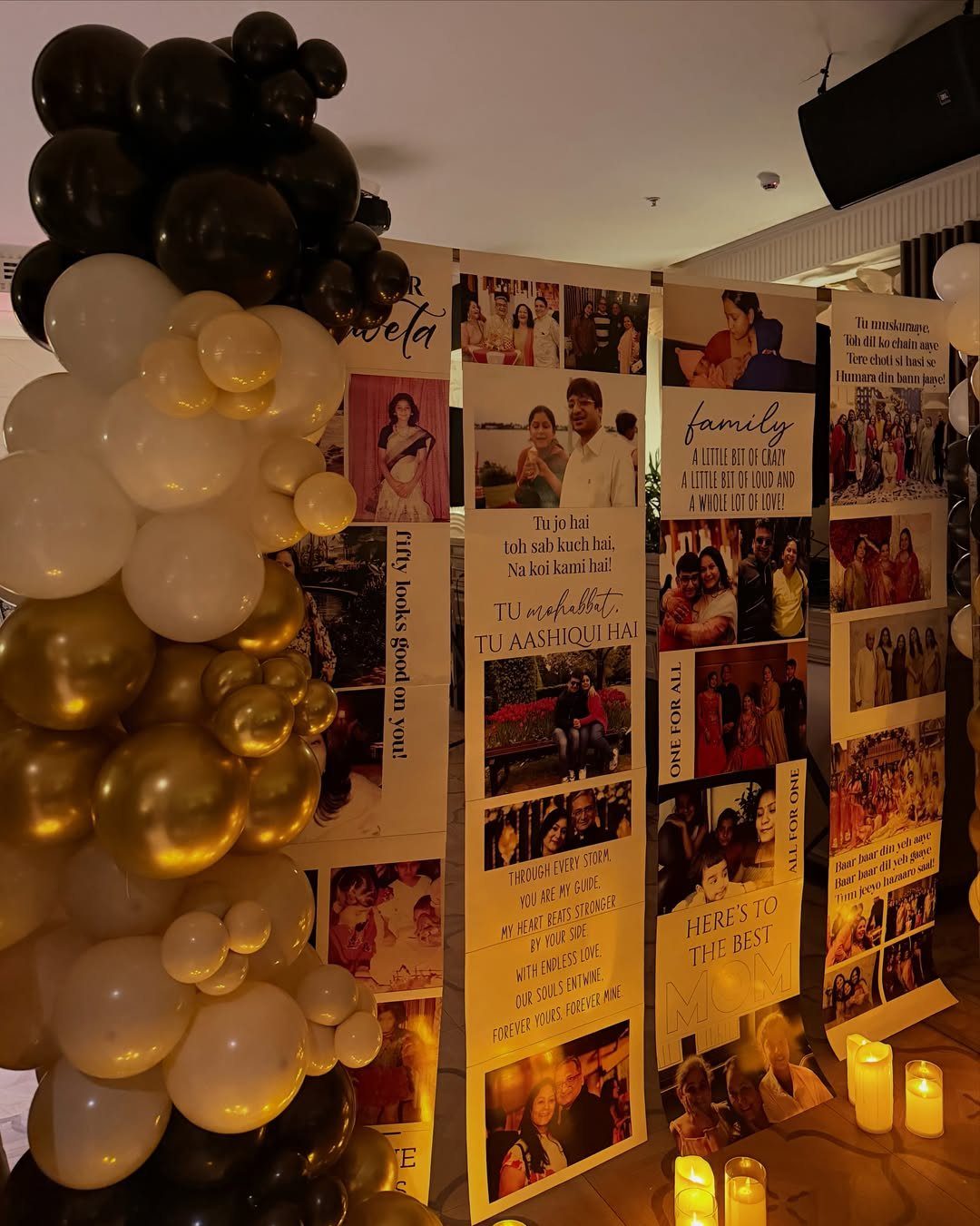 A photo display wall with personal pictures and text next to a black, white, and gold balloon arch.