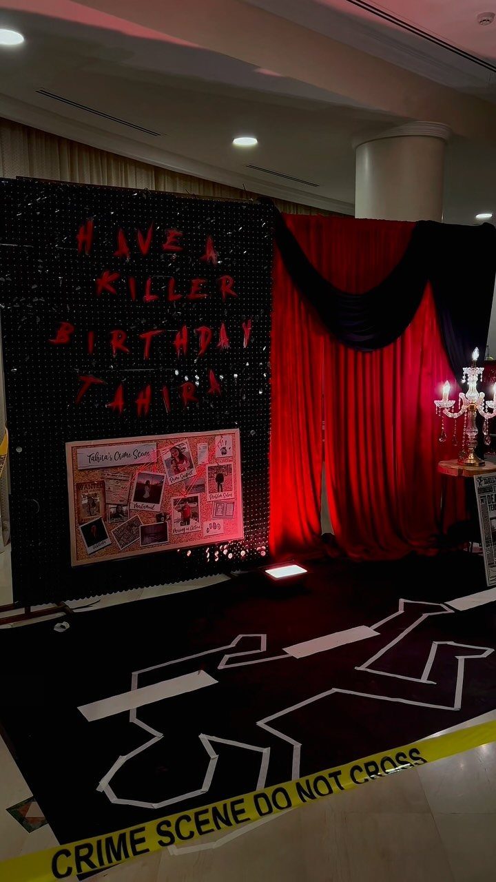 Crime scene party decorations with a body outline, yellow tape, and a black sequin backdrop.