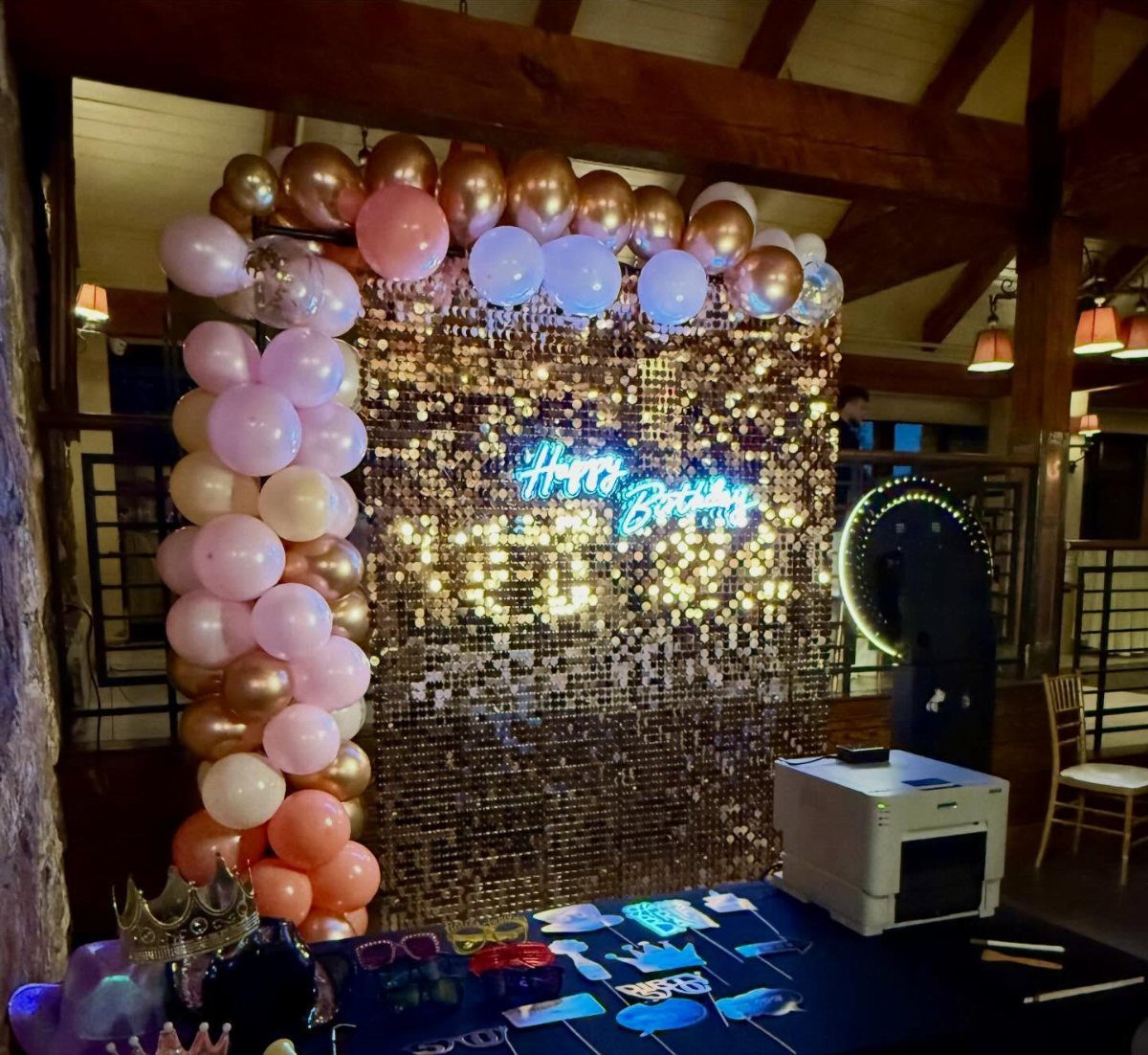 Gold sequin backdrop with a colorful balloon arch and a glowing neon birthday sign.