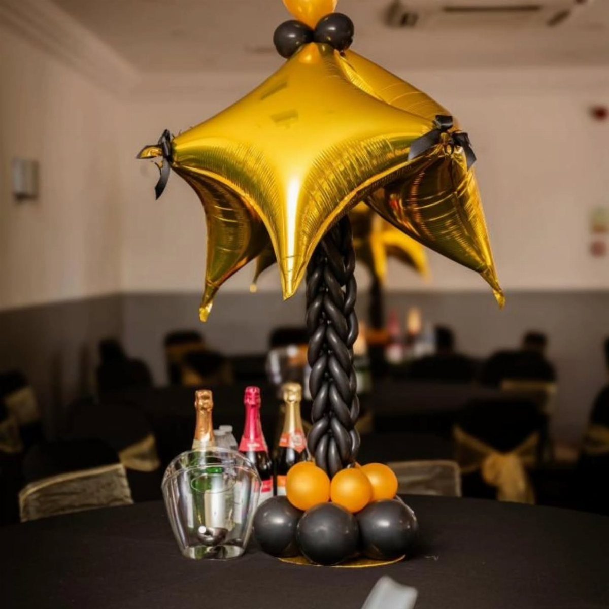 Gold star balloon centerpiece on a black braided stand with orange and black balloons on a table.