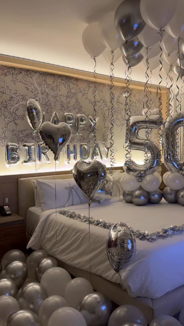 Silver and white balloons decorate a bedroom with large foil balloons spelling Happy Birthday 50.