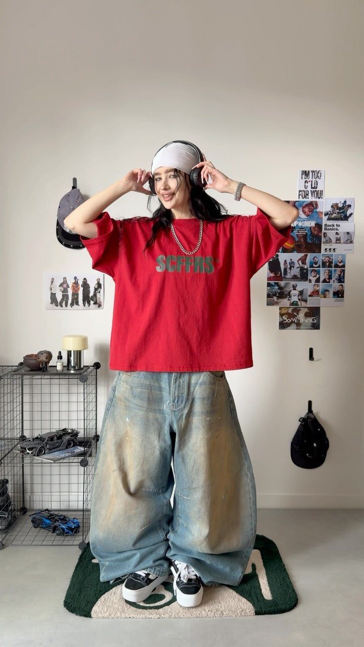 Woman wearing a red graphic t-shirt and very oversized light blue baggy jeans.
