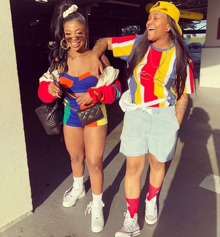 Two women in colorful retro outfits posing together while wearing bright red socks and white sneakers.