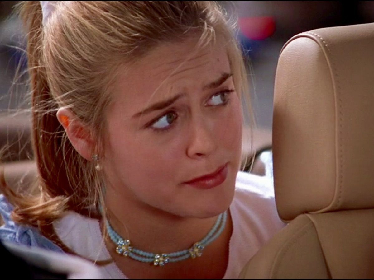A blonde woman wearing a light blue beaded choker necklace while sitting in a car.