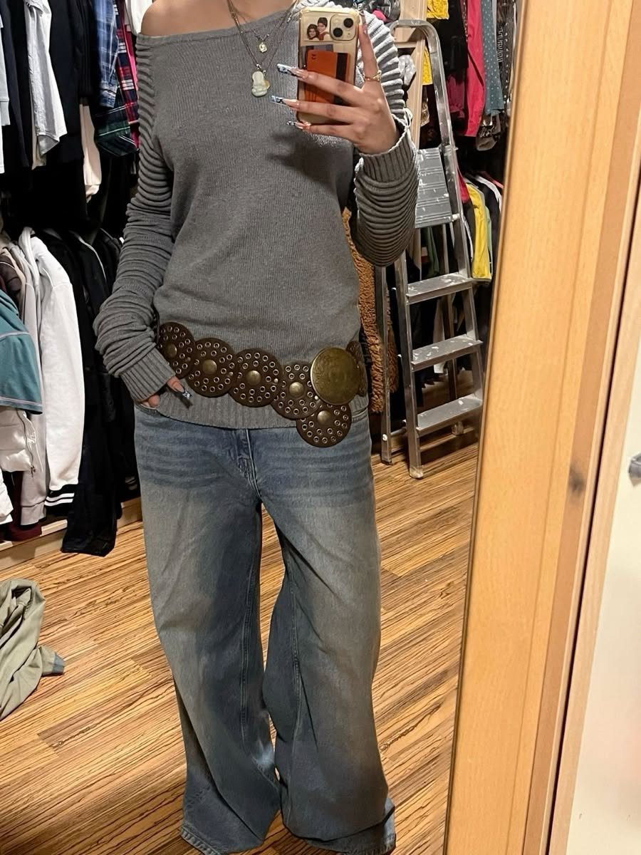 Person wearing a grey top, flared jeans, and a large brown studded chunky belt.