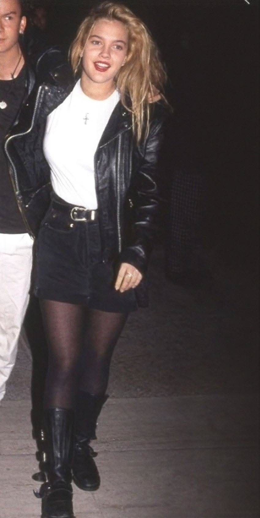 Blonde woman in a leather jacket, mini skirt, and black combat boots walking at night.