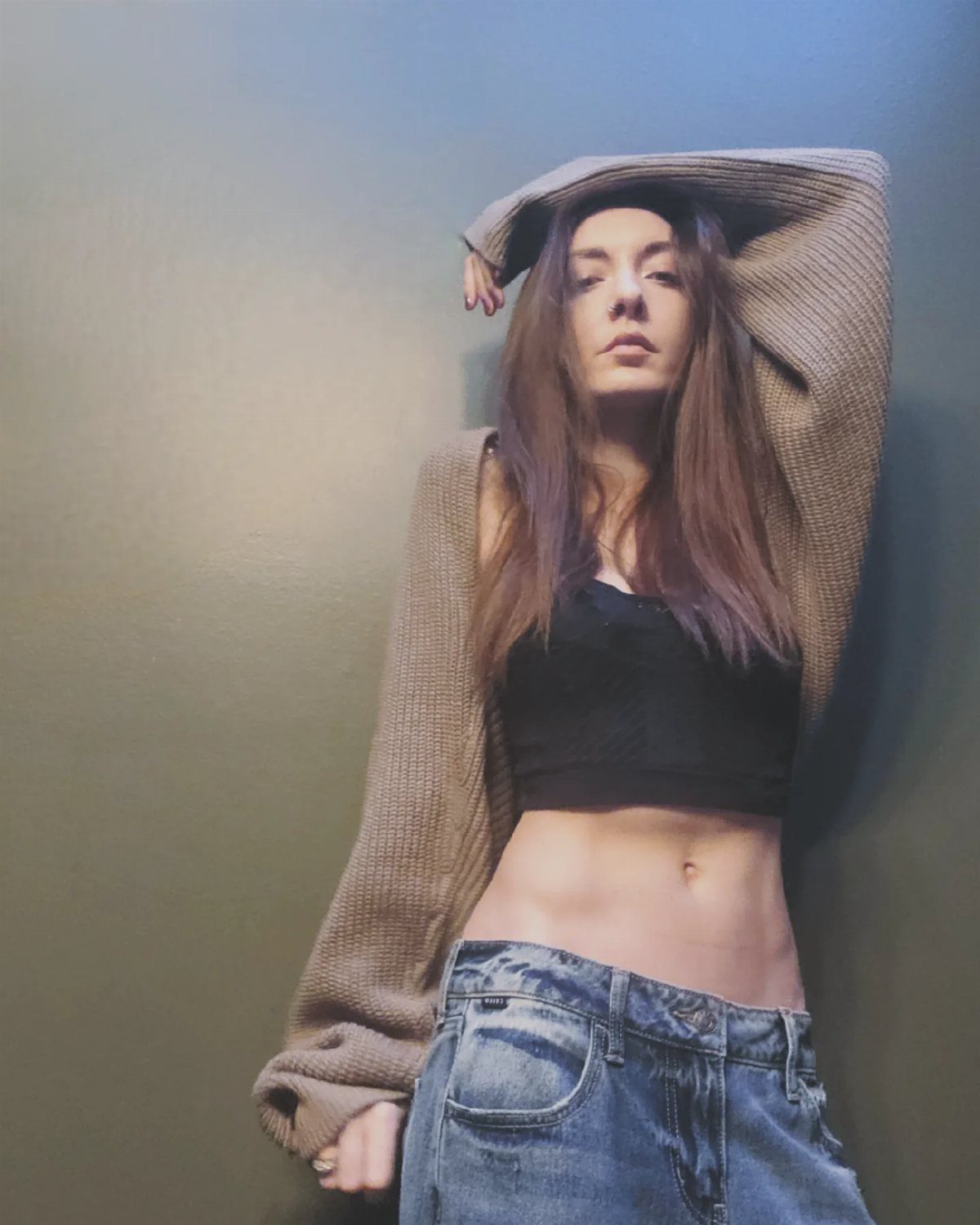 Woman wearing a black crop top and low-rise denim jeans against a dark wall.
