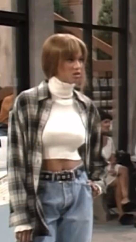 Woman wearing a white turtleneck crop top, blue jeans, and an open plaid flannel shirt.