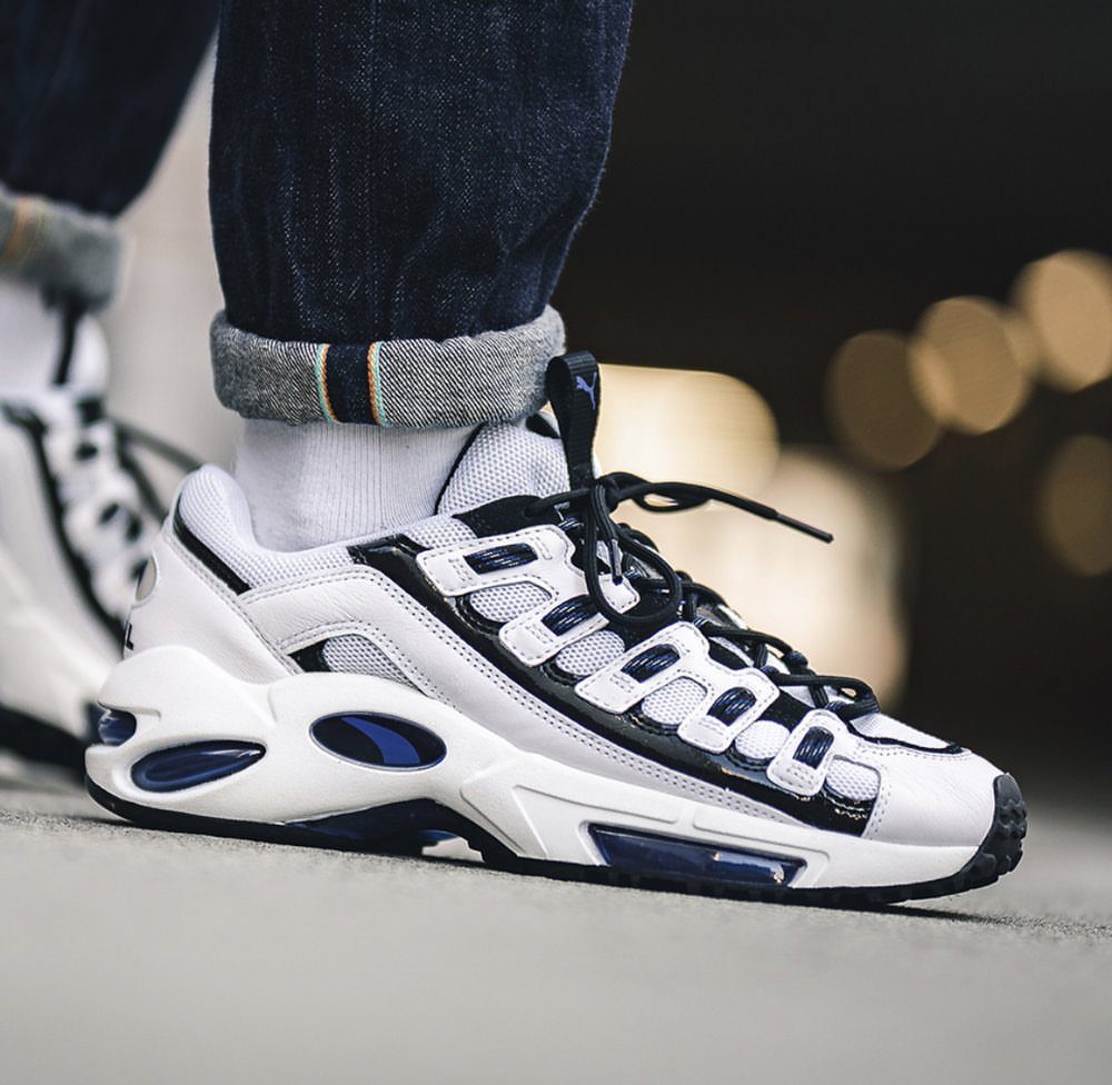 White chunky sneakers with black and blue details worn with white socks and cuffed denim jeans.