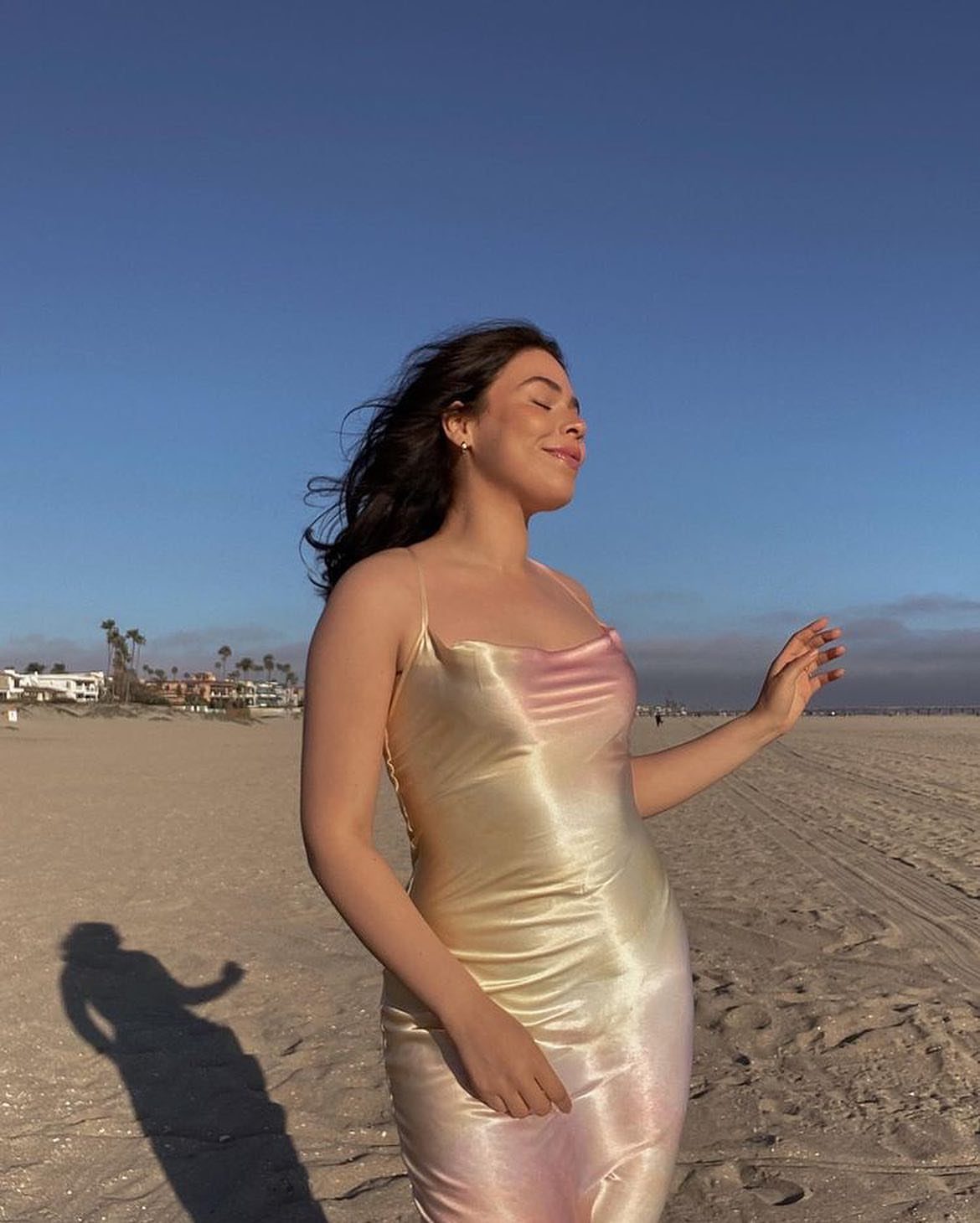Woman in a shimmering gold and pink satin slip dress standing on a sunny beach.
